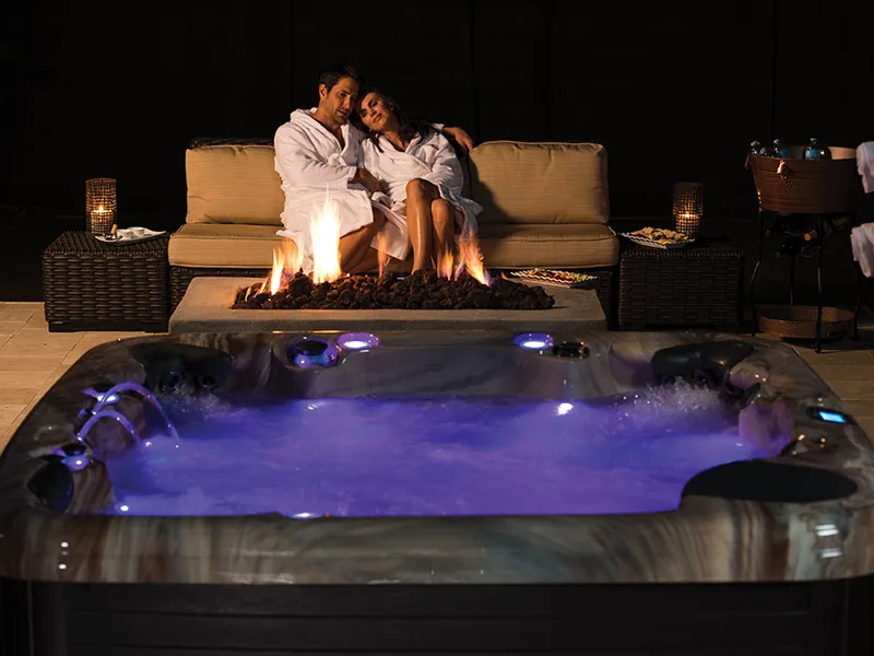 Illuminated swim spa next to an outdoor fire pit seating area at night